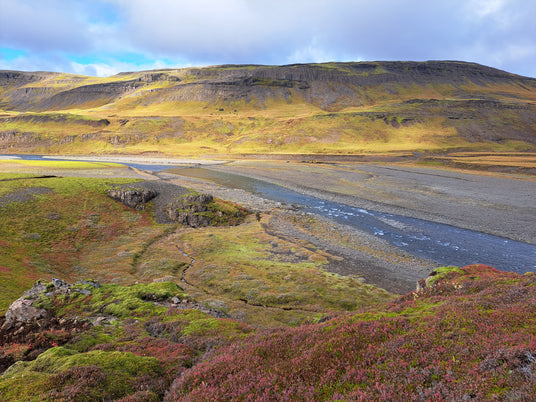 En flod rinner genom en bred, stenig dal med gröna kullar och växtlighet-perfekt plats för sportfiske på fiskeresa.