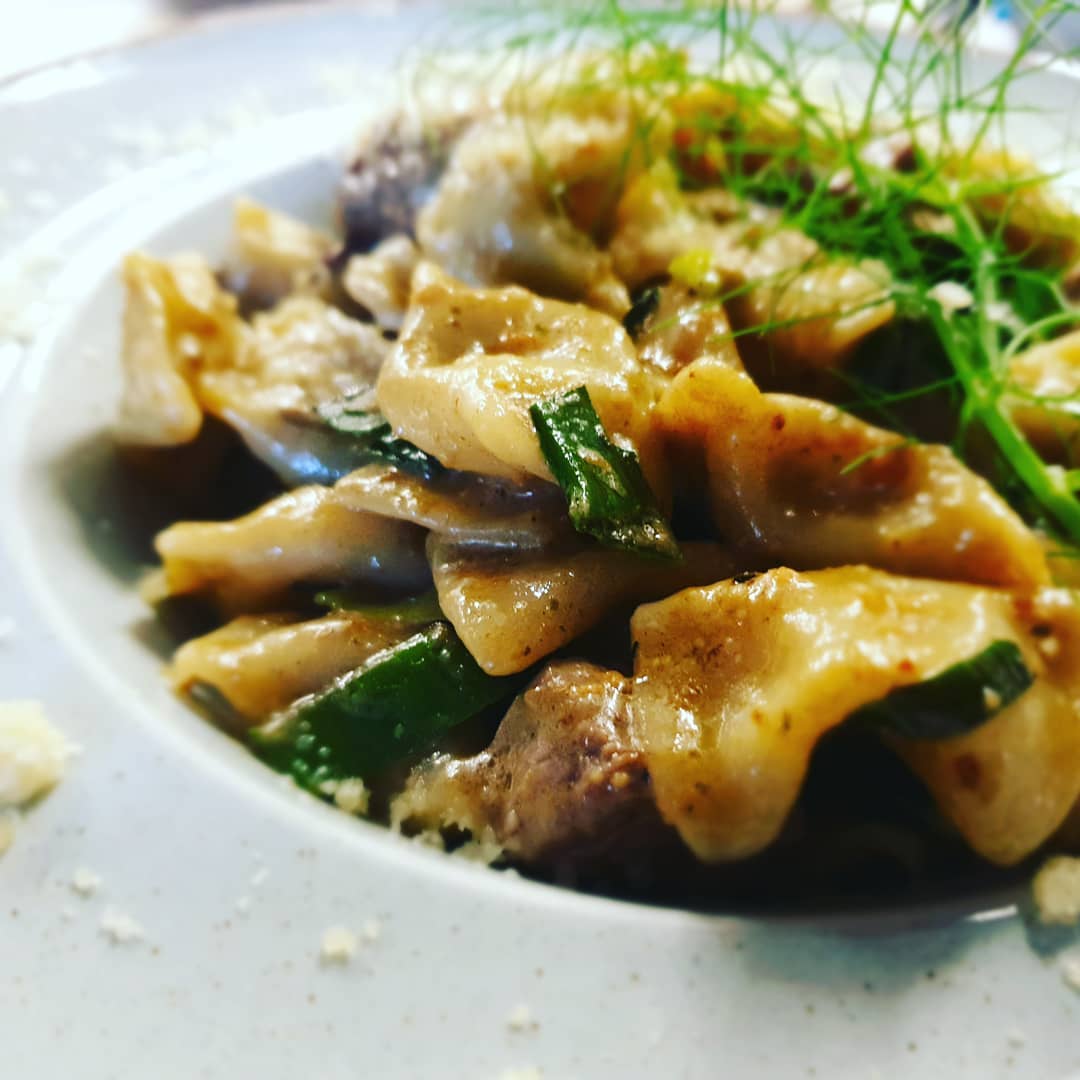 Närbild av pasta med krämig sås, gröna grönsaker och fänkål på vit tallrik-idealisk måltid för sportfiskeäventyr.