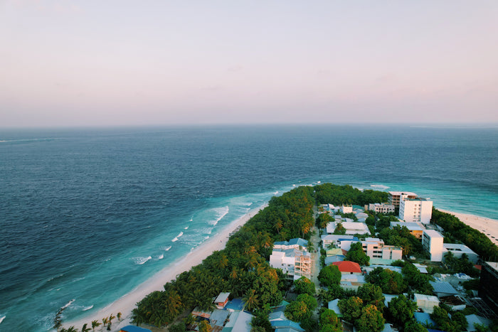 Flygfoto över tropisk öby bland palmer och turkost hav, idealisk för sportfiskeäventyr med synliga byggnader och slingrande vägar.