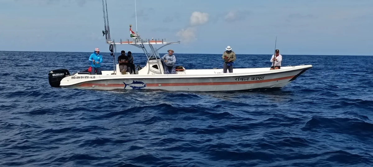Vit fiskebåt med fem personer på djupt blått hav under klar himmel. Två sportfiskare fiskar, utrustning synlig ombord.