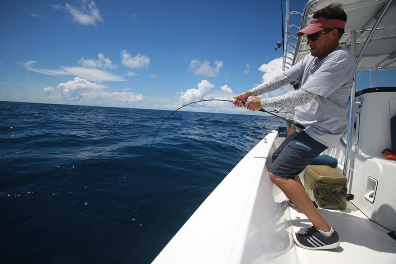 Sportfiskare med solglasögon och keps fiskar från båt, drar upp fångst över öppet hav-en inspirerande fiskeresa.