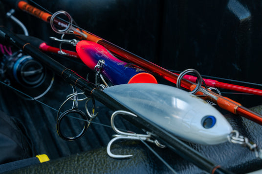 Närbild på fiskespön med färgglada beten och krokar, redo för fiskeresa, placerade i flaket på en svart pickup.