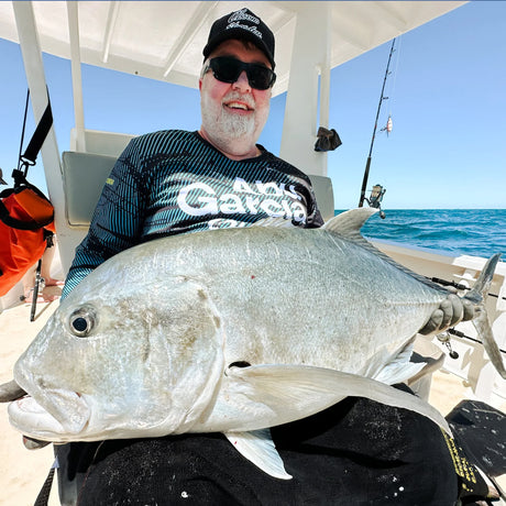 Leende sportfiskare med solglasögon och keps håller stor fisk på båt, fiskeutrustning, blått hav-Fiskeresa Madagaskar.