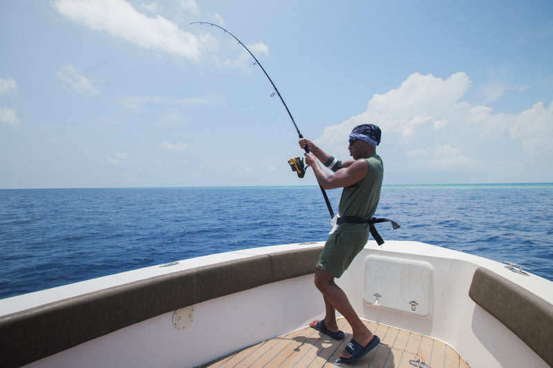 Sportfiskare i grön linne fiskar från båt på öppet hav, drar upp fisk med spö under molnig himmel - äventyr på fiskeresa.