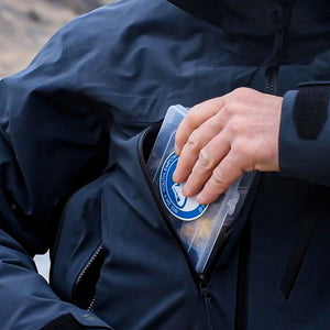 In field image of a fly box being placed into a zippered chest pocket.