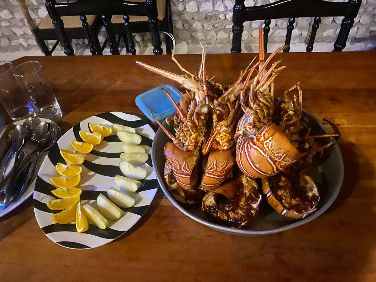 Stor skål med hela kokta humrar på träbord, citron- och limeklyftor bredvid-idealisk måltid efter lyckad fiskeresa.