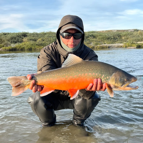 Sportfiskare vid Camp Qussuk, Grönland, håller en stor fisk i vattnet. Fiskeupplevelse med natur och blå himmel runtom.
