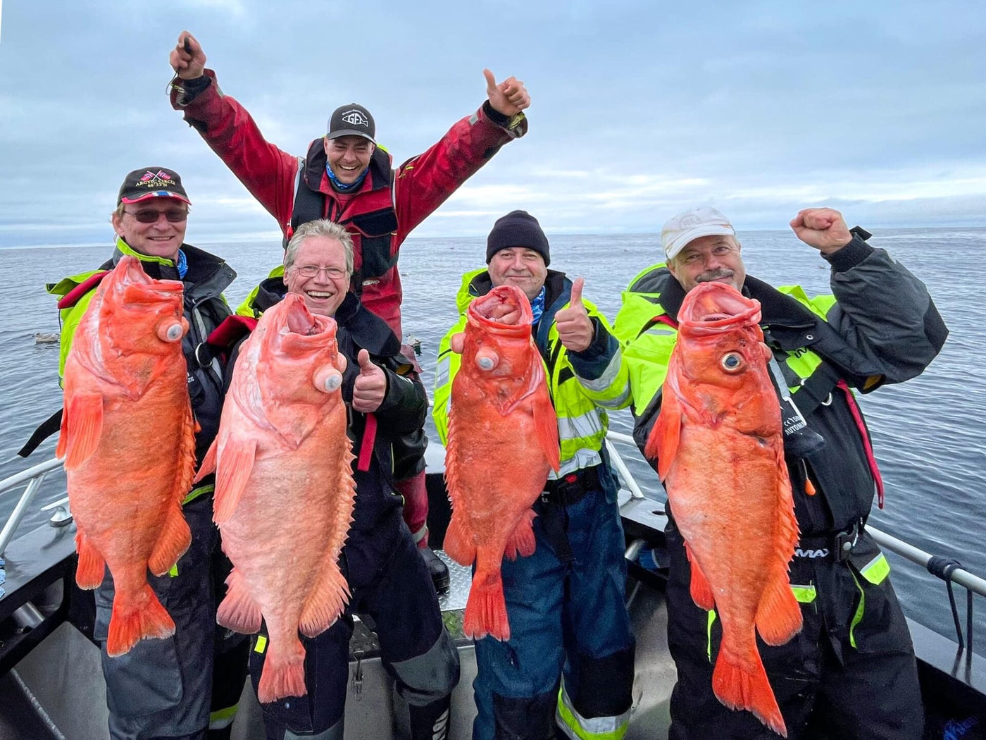 Fem sportfiskare på båt visar stolt upp stora orange fiskar med havet i bakgrunden under sin fiskeresa.