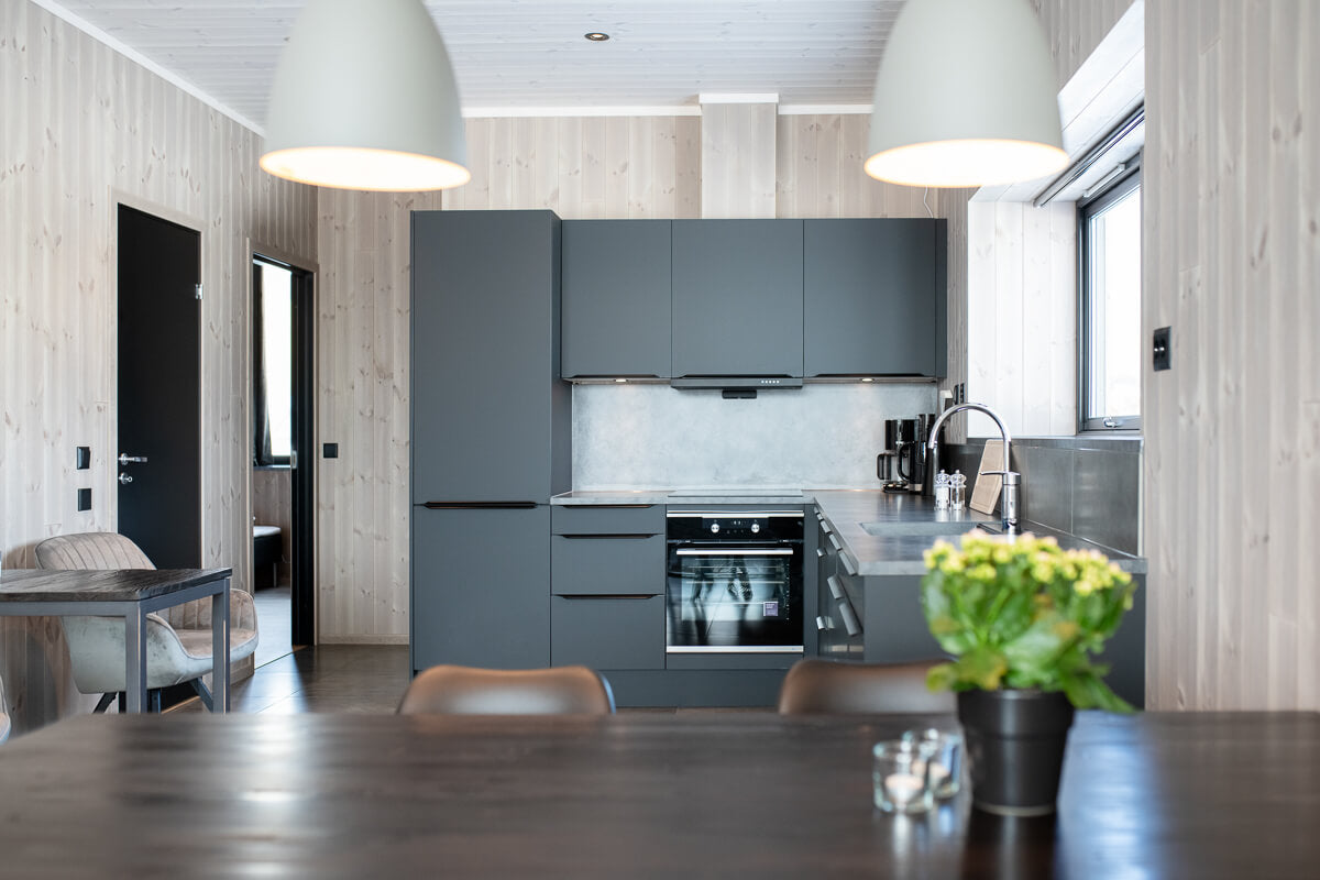 Modernt grått kök med träpanel, ljus pendellampa och växt på bänken. Perfekt plats för sportfiskare att koppla av efter fiskeresan.