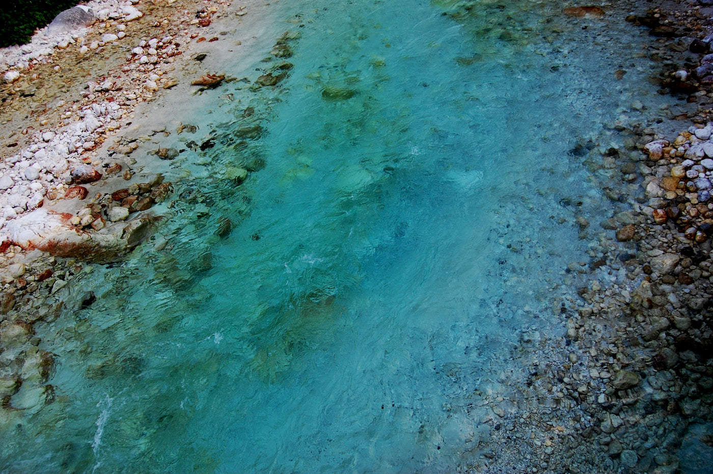 Klart turkost vatten rinner över släta stenar i en grund bäck-en idealisk plats för sportfiske och naturupplevelser.