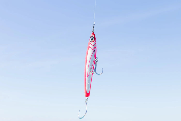 Ett rött och vitt fiskedrag med två trekrokar hänger från en lina mot blå himmel, redo för nästa sportfiskeäventyr.